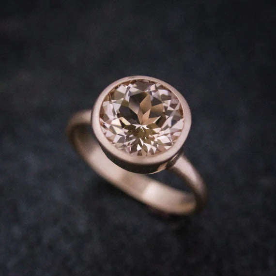 A close-up image of a silver ring with a large, round, faceted gemstone set in a bezel setting, displayed on a dark surface.
