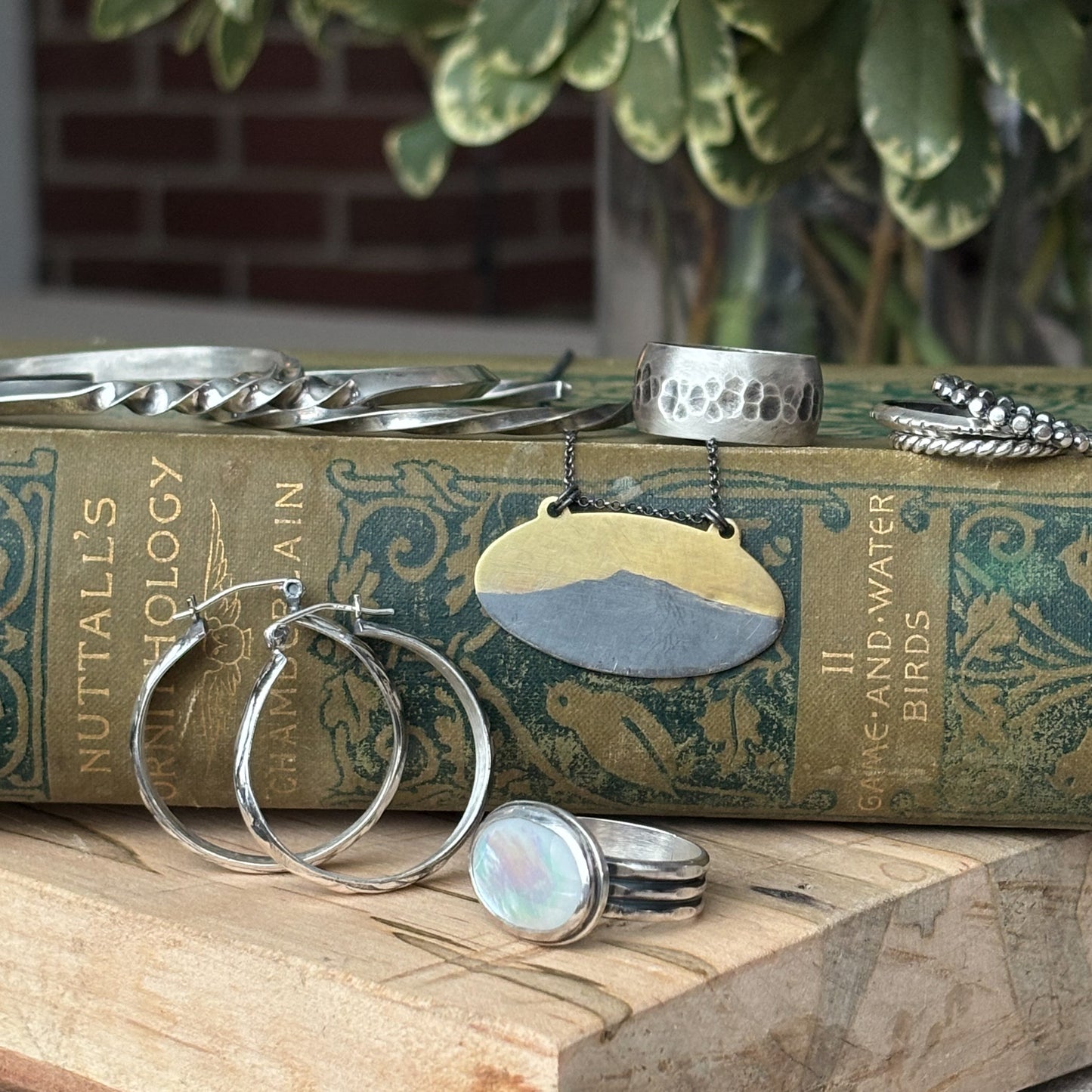 Displayed on a vintage green book, the collection features a pendant necklace, hoop earrings, and a Custom Milestone Sapphire Ring in sterling silver, beautifully complemented by a stunning blue sapphire cabochon.