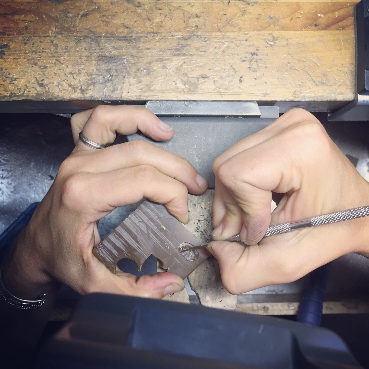 Hands intricately carve a heart into 14k white gold using precision tools, reflecting the craftsmanship needed for creating a Black Spinel and White Gold Split Shank Ring, where every detail requires meticulous attention and artistry.