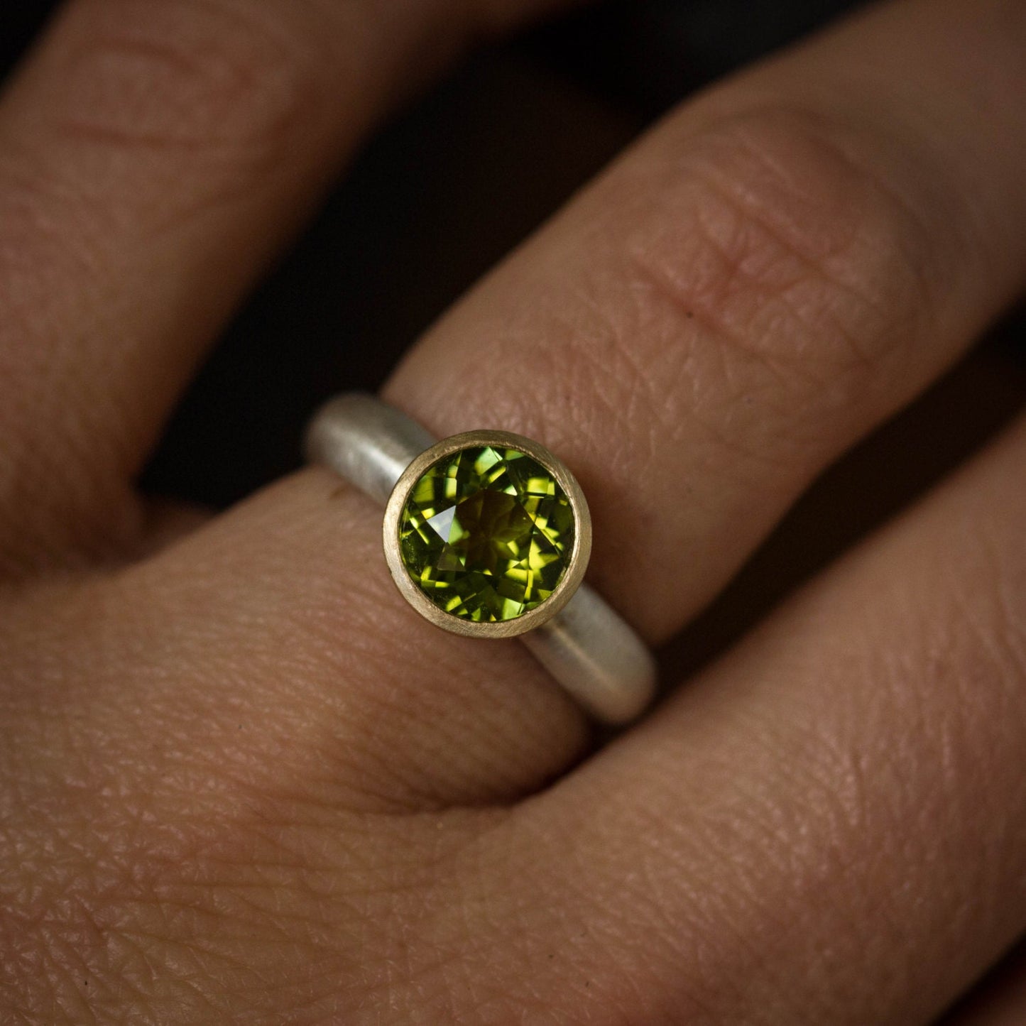A woman's hand holding a handmade Peridot Mixed Metal Gemstone Ring from Cassin Jewelry.