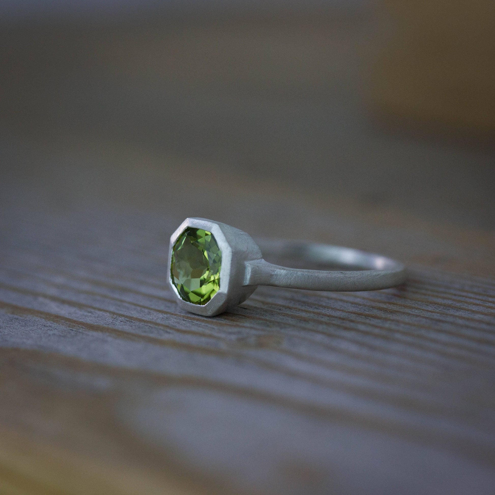 A handmade Peridot Ring in August Birthstone on a wooden table.
