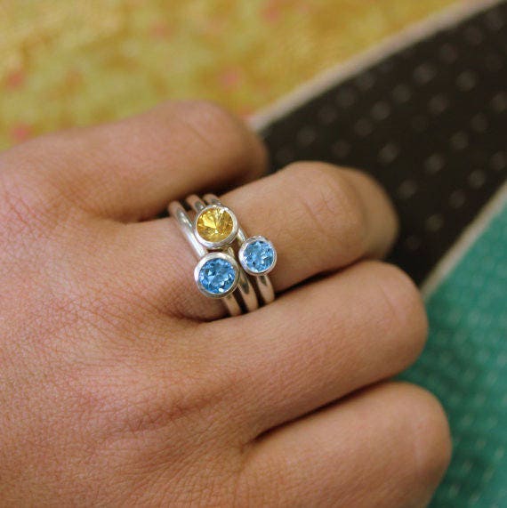 A hand wearing three Argentium Sterling silver stacking rings—set with peridot, amethyst, and iolite gemstones—perfect as a modern Mother’s Ring.
