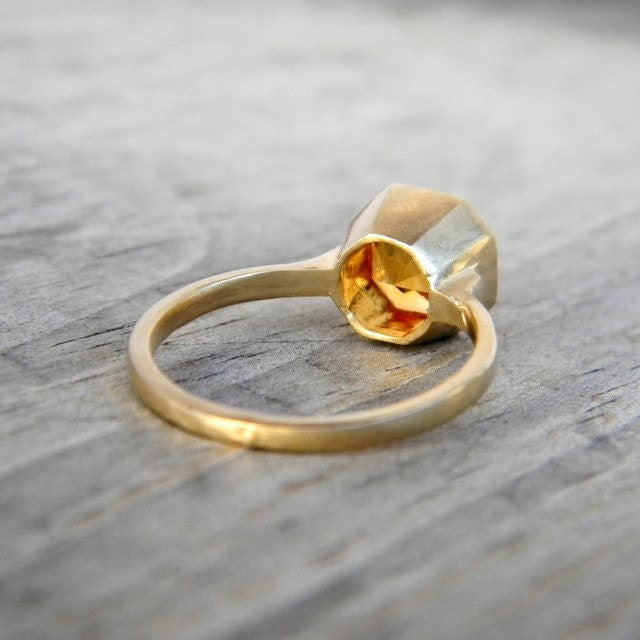 The Citrine Gemstone Bezel Ring in Asscher Cut 14k yellow Gold features a beautifully cut citrine set in a hexagonal bezel, elegantly displayed on a wooden surface.