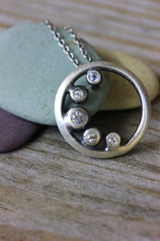 A handmade white sapphire cresent moon pendant necklace with a diamond in the middle by Cassin Jewelry.