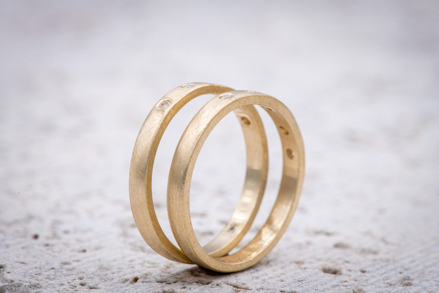Two handmade Moissanite Gold Wedding Bands on a concrete surface.