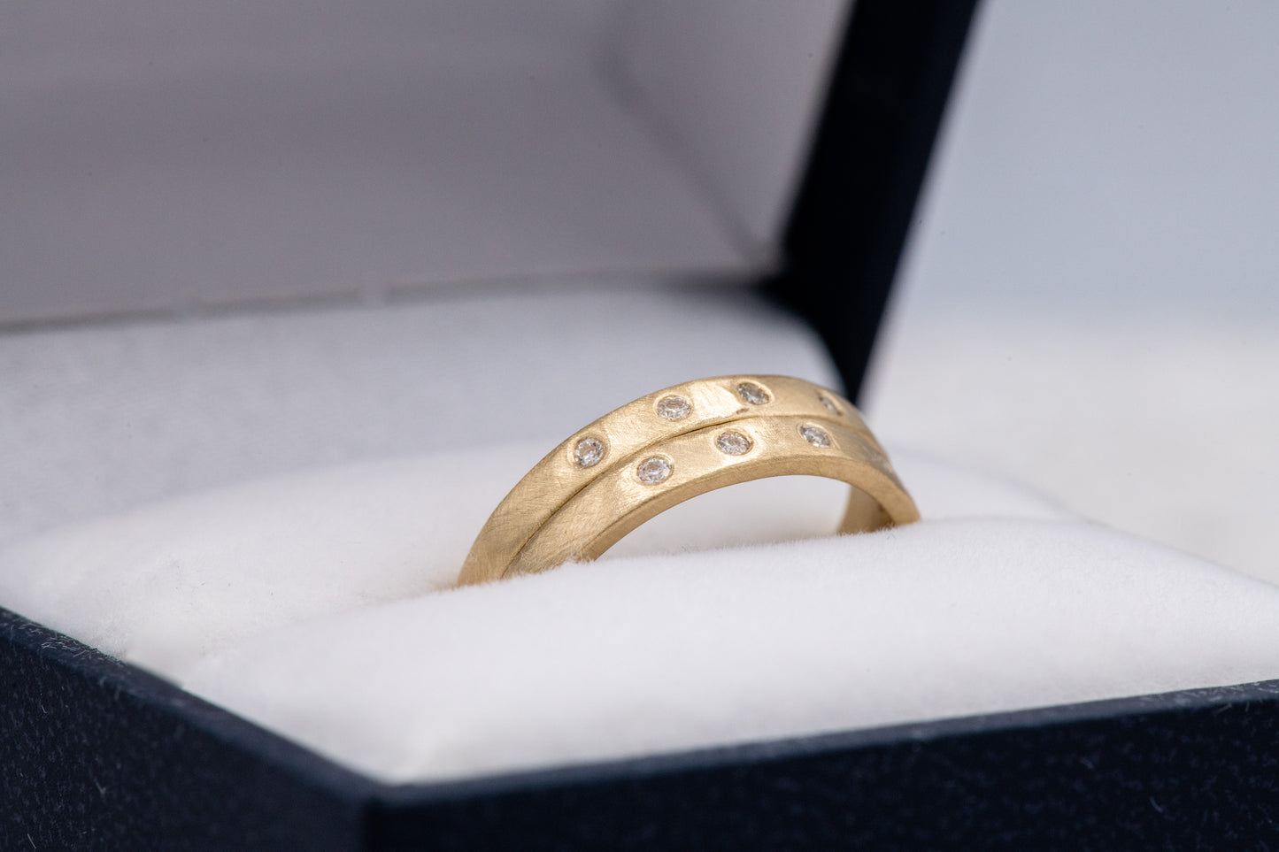 A handmade Moissanite Gold Wedding Band with diamonds in a box by Cassin Jewelry.