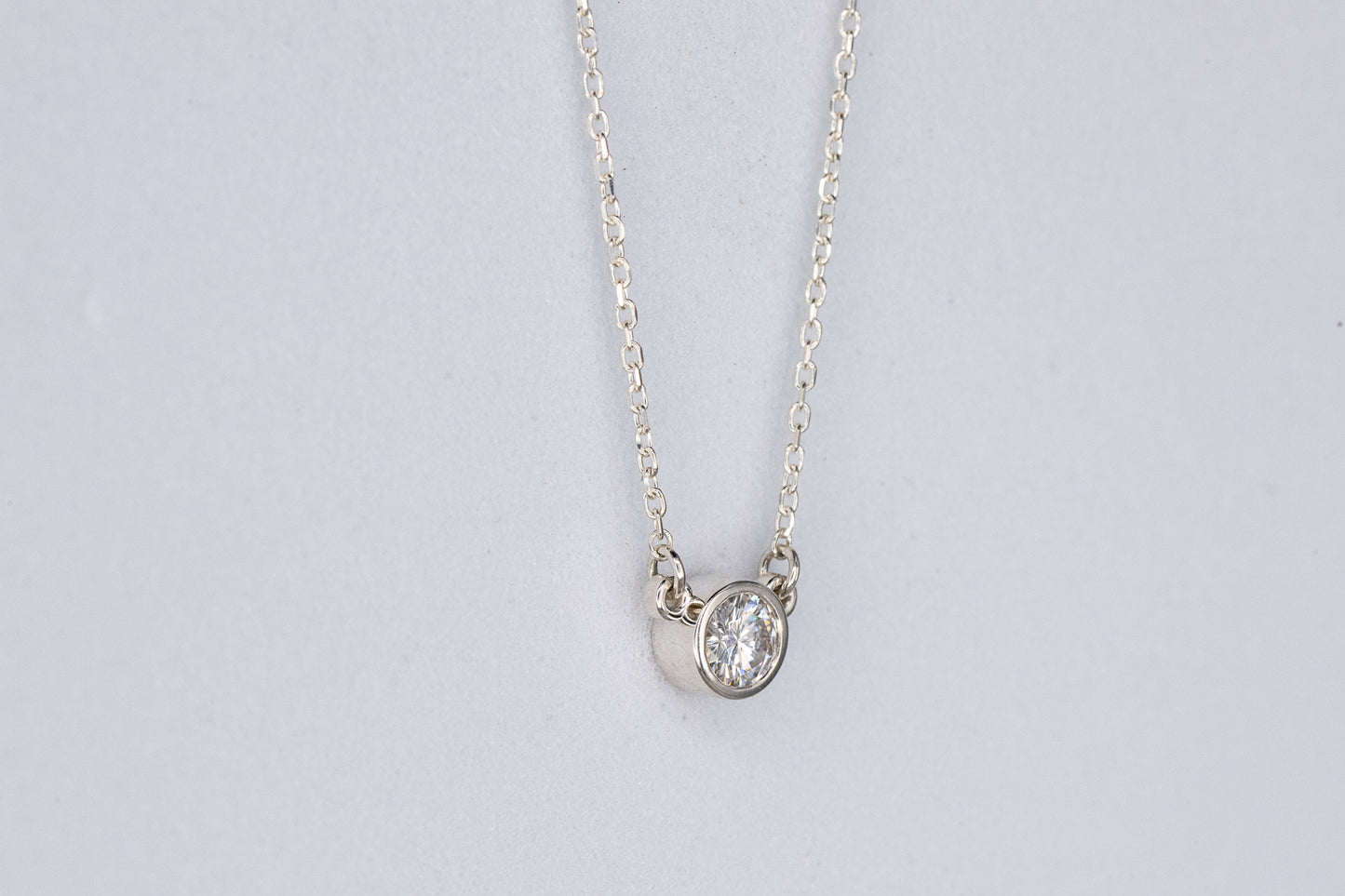 A Moissanite Sterling Silver Necklace with a small diamond, handmade by Cassin Jewelry.