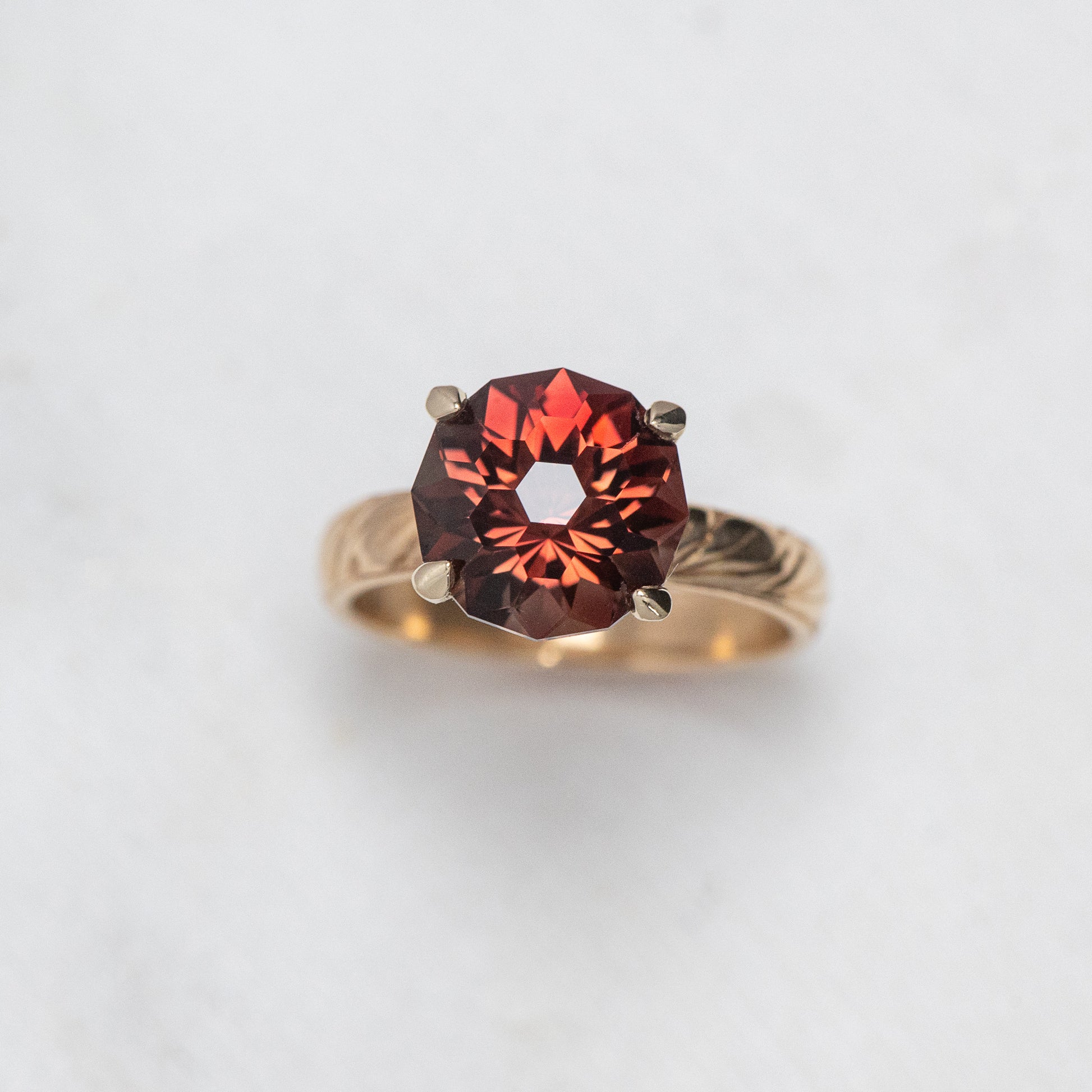 A One of A Kind Custom Handcrafted Oregon Sunstone Ring in 14k Yellow Gold Size 7 with an intricate band and a large, round red gemstone set in a prong setting, placed on a light marble surface.