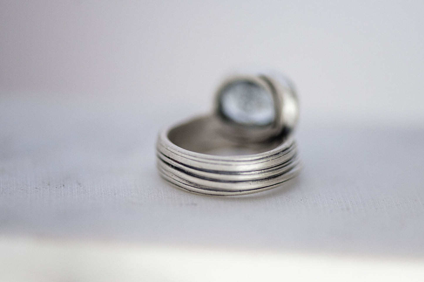 Close-up of the One of A Kind Oval Moss Aquamarine Ring in size 9.5, featuring multiple thin sterling silver bands stacked together. An oval aquamarine gemstone sits gracefully at the top, with the background softly out-of-focus.