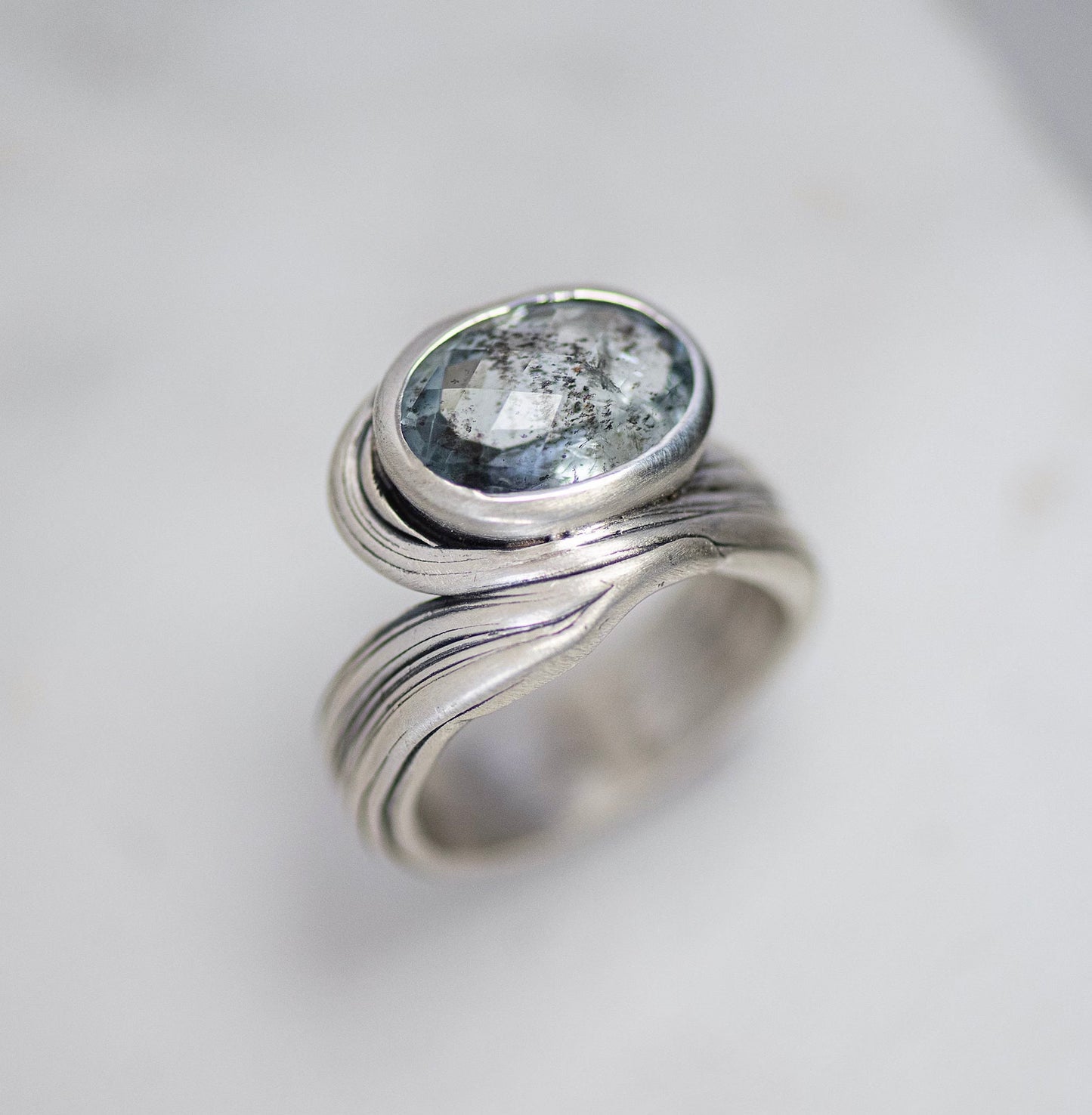 The One of A Kind Oval Moss Aquamarine Ring - Size 9.5 boasts a stunning, light blue Moss Aquamarine gemstone in an oval shape, set within a layered and textured sterling silver band, exemplifying the finest in handmade jewelry craftsmanship.