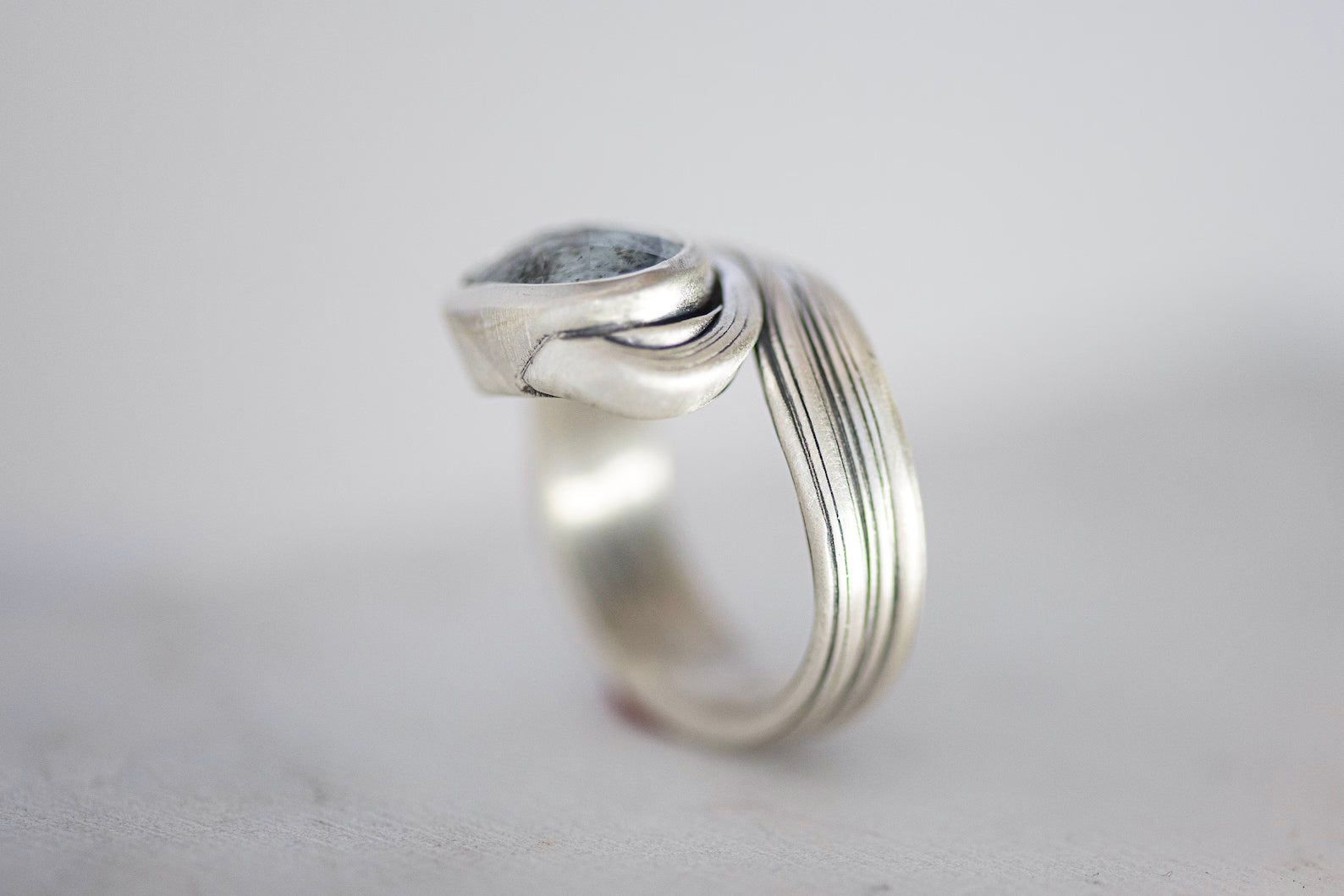 A unique, one of a kind ring featuring an oval Moss Aquamarine gemstone set in a layered design with a chunky, textured sterling silver band, available in size 9.5.