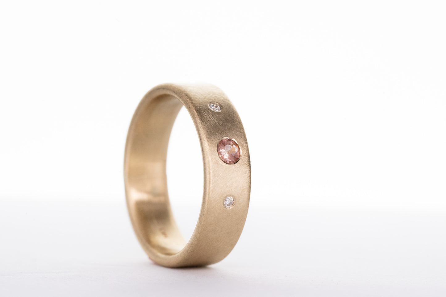 A handmade Oregon Sunstone and Diamond wedding ring with pink diamonds, crafted by Cassin Jewelry.