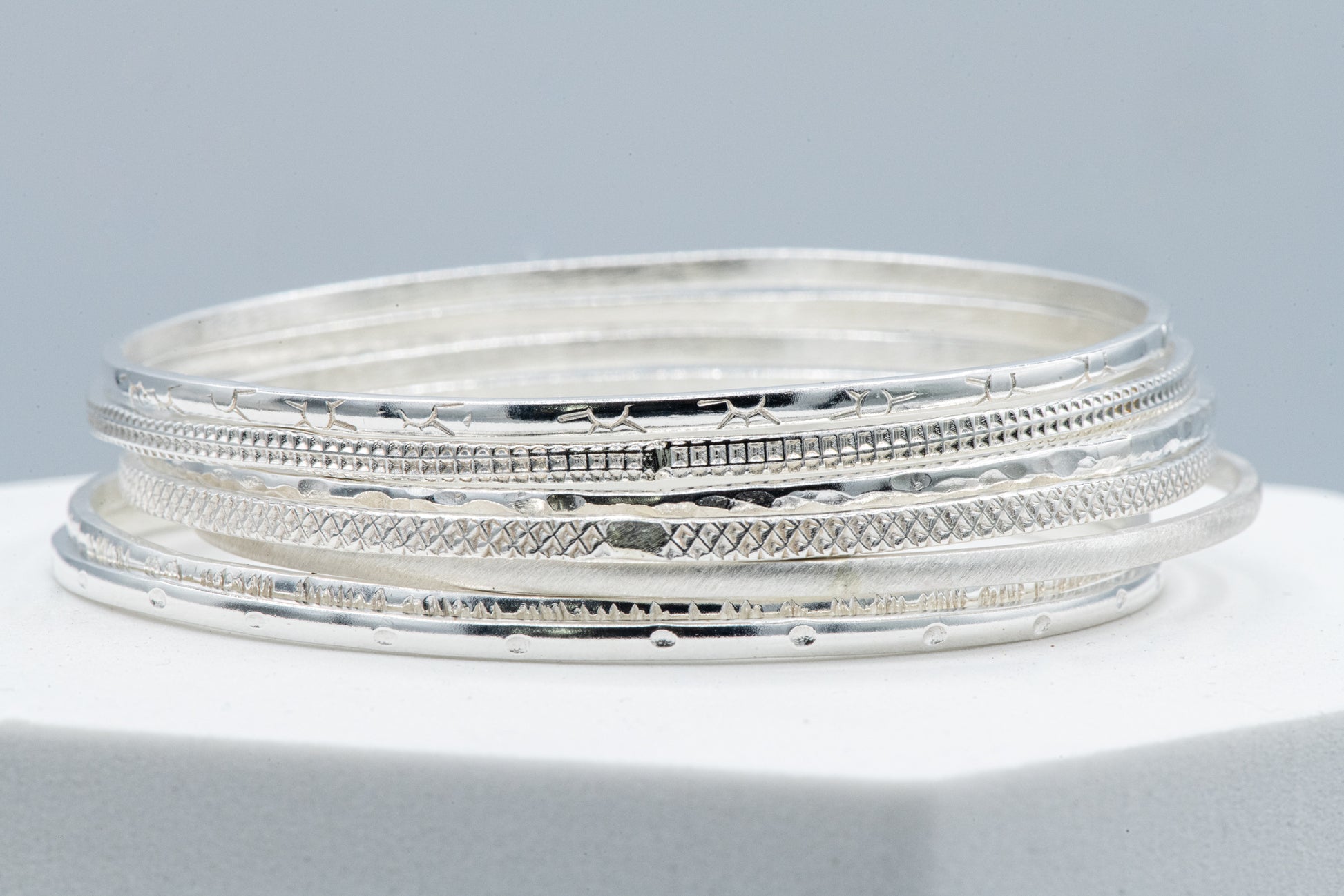 A set of seven handmade sterling silver bangles on top of a square.