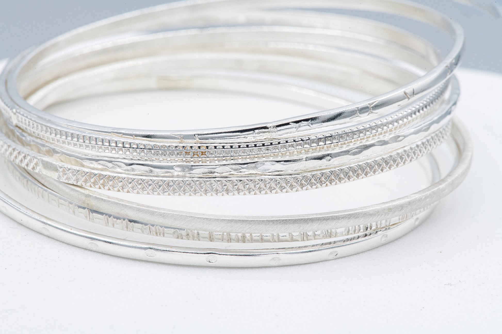 A set of seven handmade sterling silver bangles on a white surface.