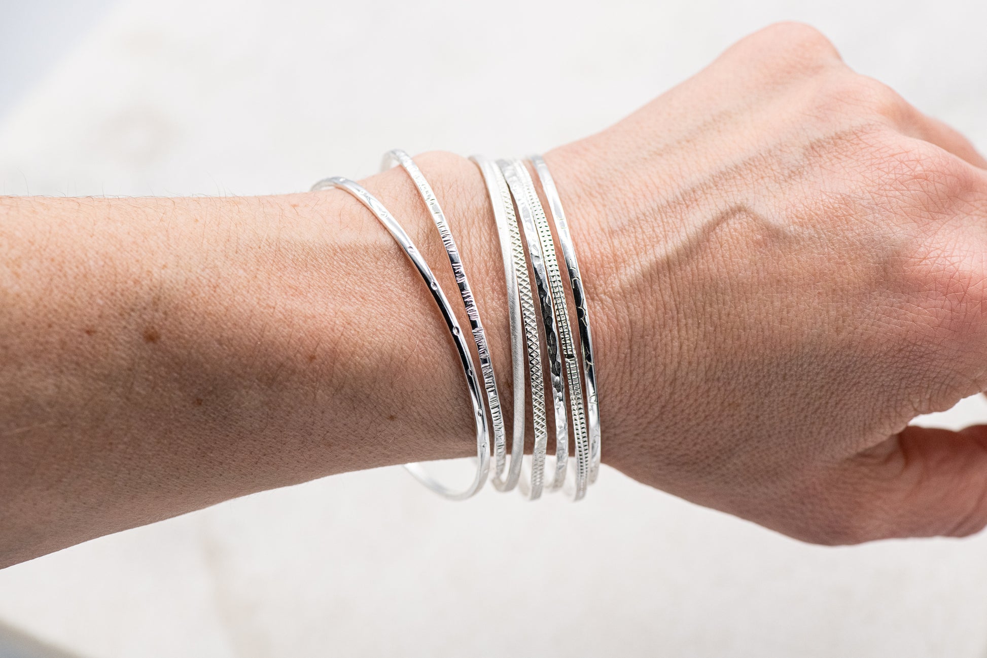 A woman's hand adorned with a set of seven handmade sterling silver bangles from Cassin Jewelry.