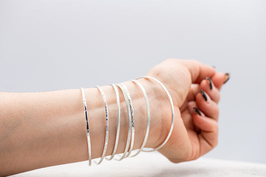 A woman's hand holding a set of seven handmade sterling silver bangles.