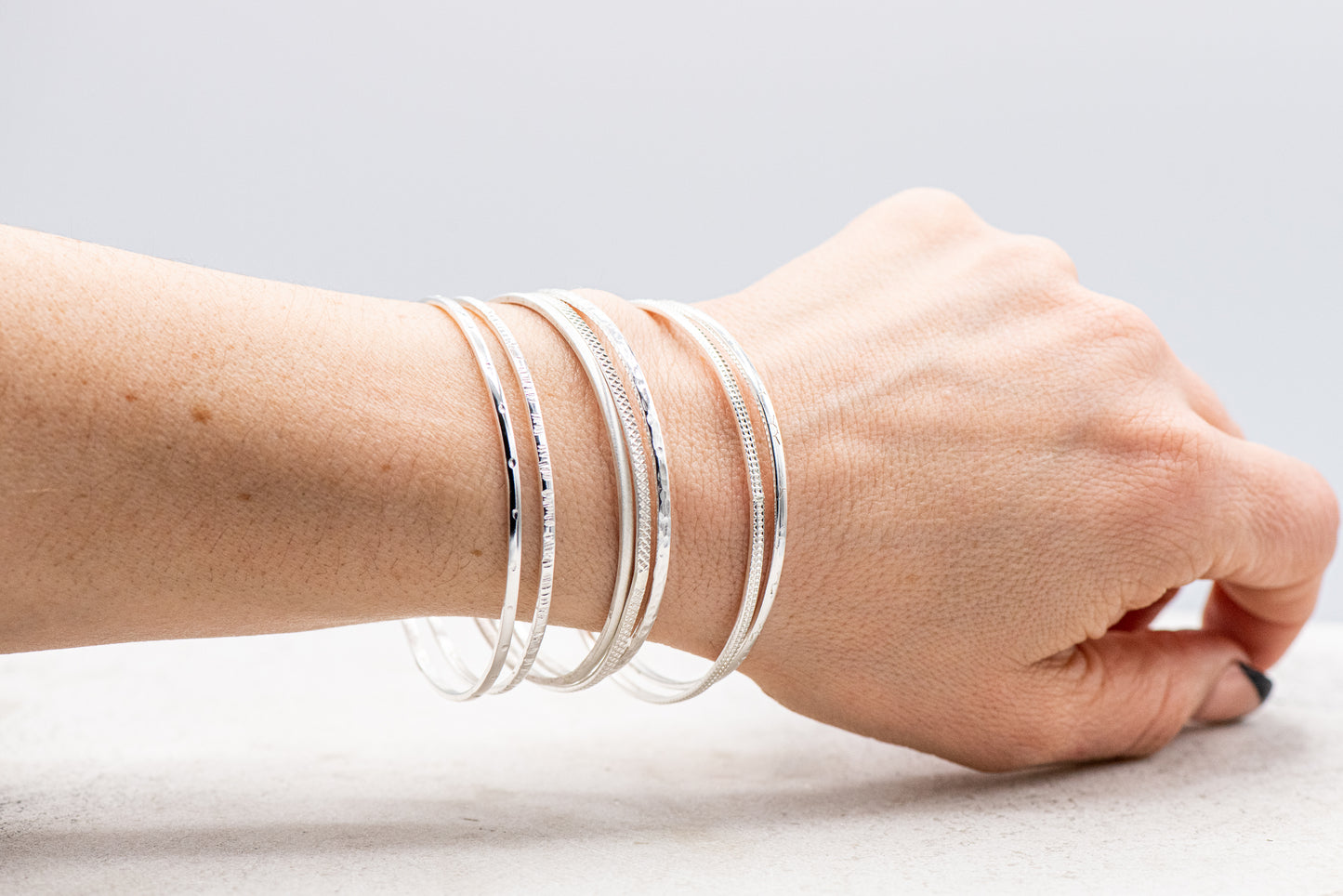 A woman wearing the Set of Seven Sterling Silver Bangles handmade by Cassin Jewelry on her wrist.