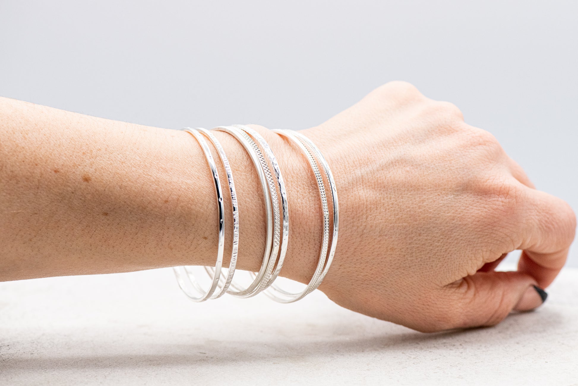 A woman wearing the Set of Seven Sterling Silver Bangles handmade by Cassin Jewelry on her wrist.