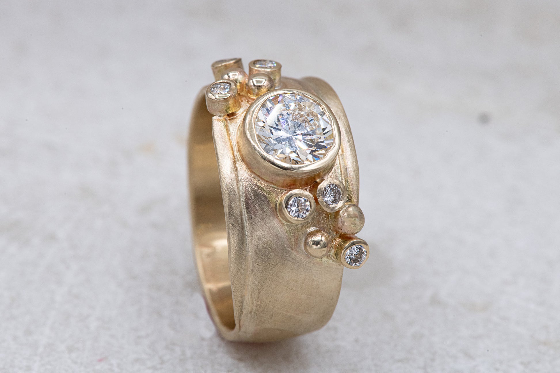 A handmade Wide Forever One Moissanite Gold Ring with a diamond in the center from Cassin Jewelry.