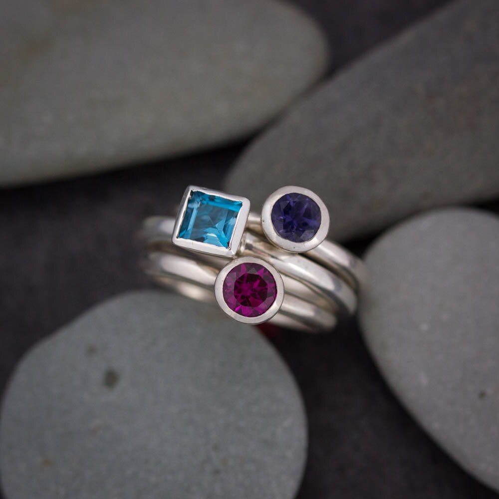 Handmade jewelry stack of Square London Blue Topaz Rings with blue and purple stones.