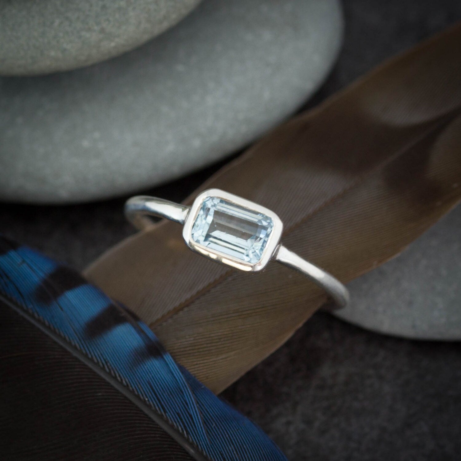 A handmade jewelry piece by Cassin Jewelry featuring a sky blue topaz stone on top of feathers, crafted with sterling silver.
