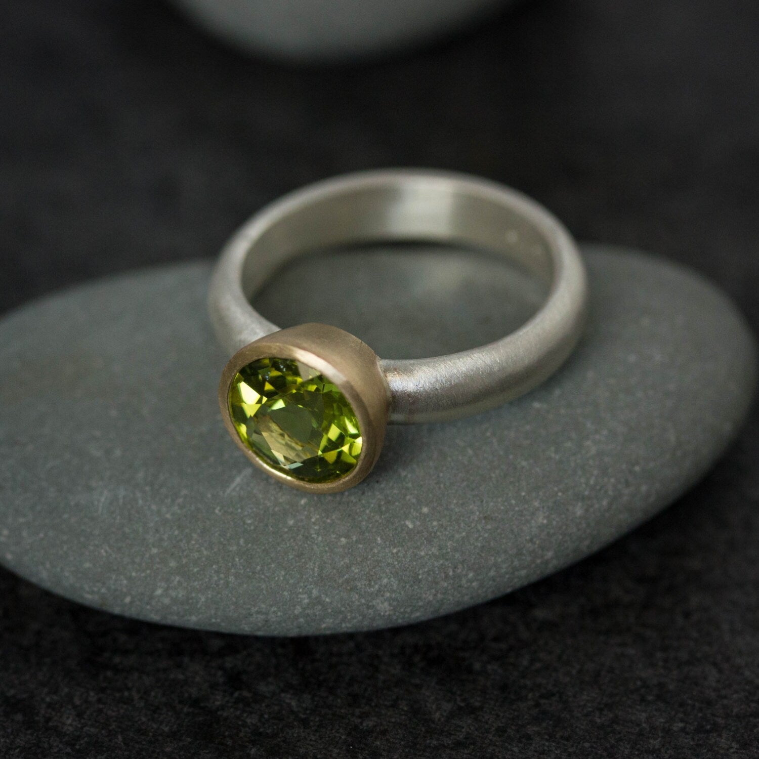 A handmade Peridot Mixed Metal Gemstone Ring with a peridot stone on top of rocks.