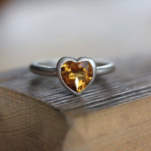 A Silver Handmade Citrine Heart Ring on top of a piece of wood by Cassin Jewelry.