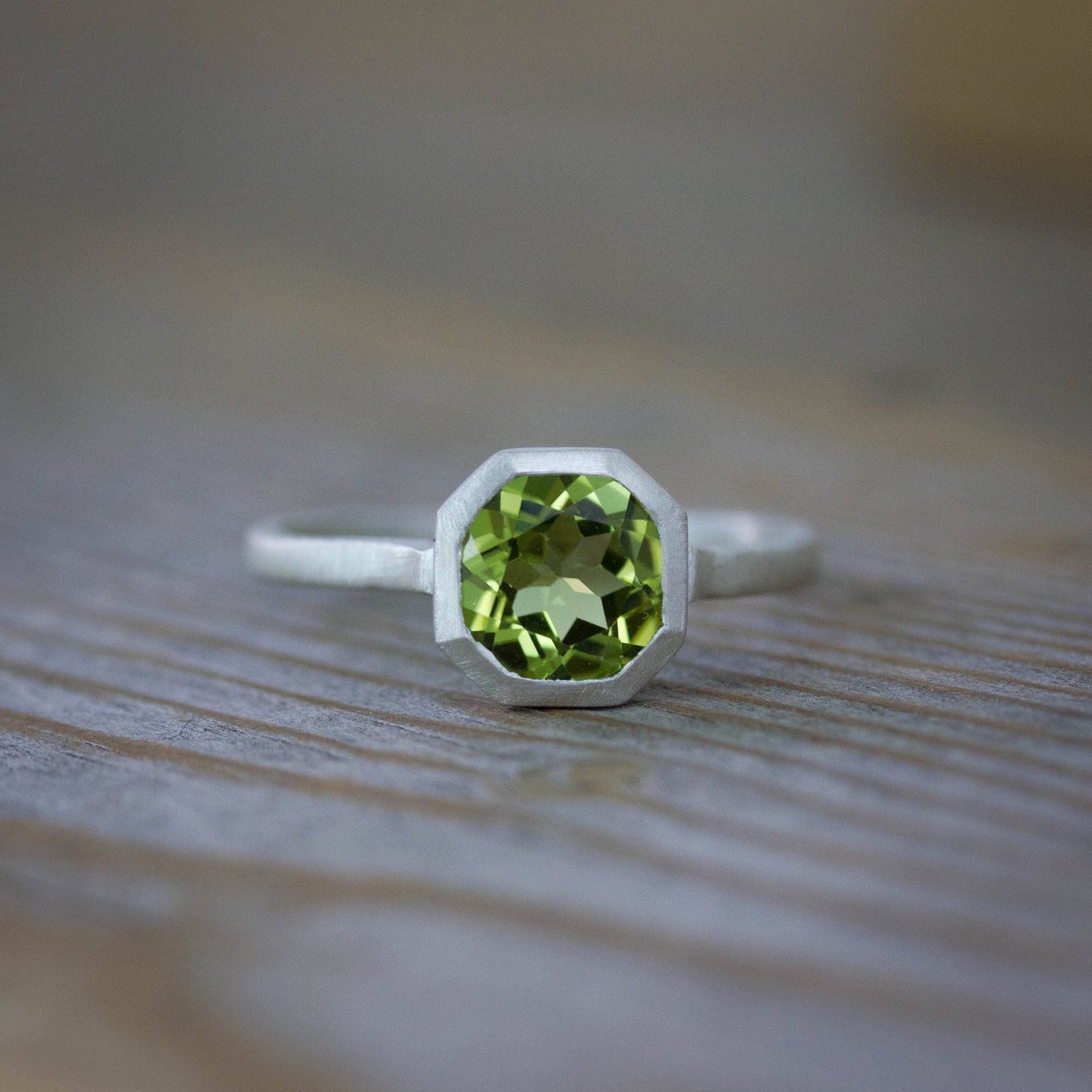 A handmade Peridot Ring in August Birthstone on a wooden table.