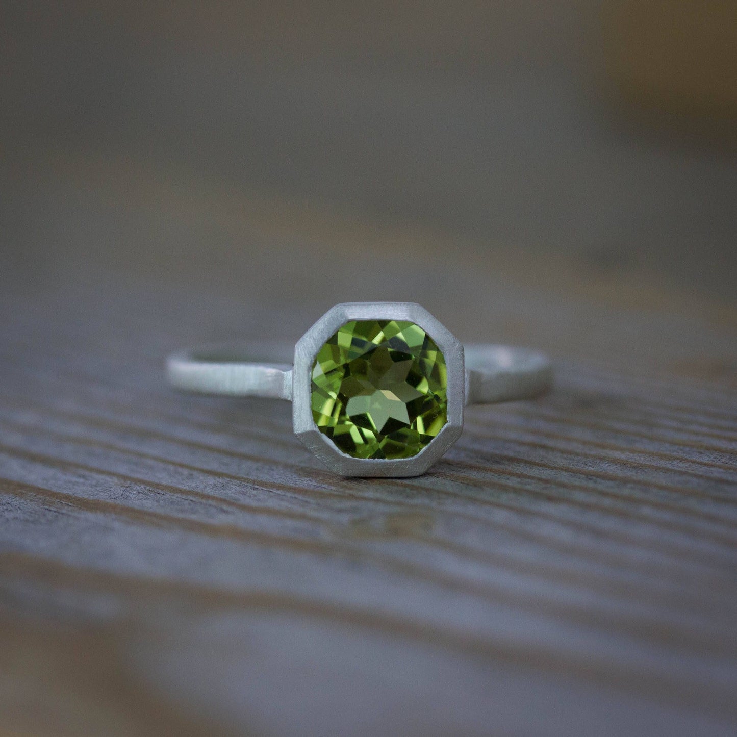 A handmade Peridot ring from Cassin Jewelry showcased on a wooden table.