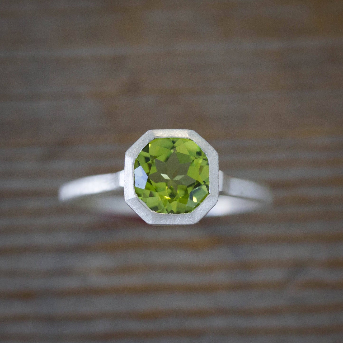 An octagonal Peridot Ring in August Birthstone on a wooden table from Cassin Jewelry.