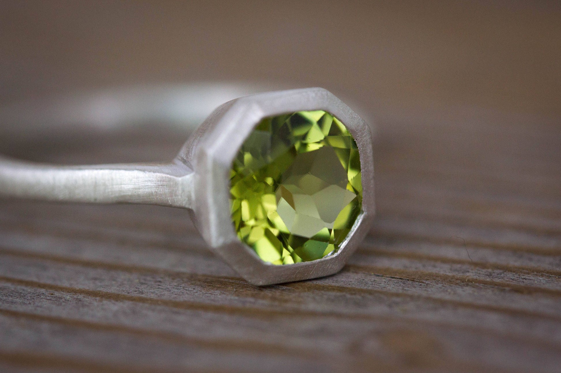 A handmade Peridot Ring from Cassin Jewelry on a wooden table.