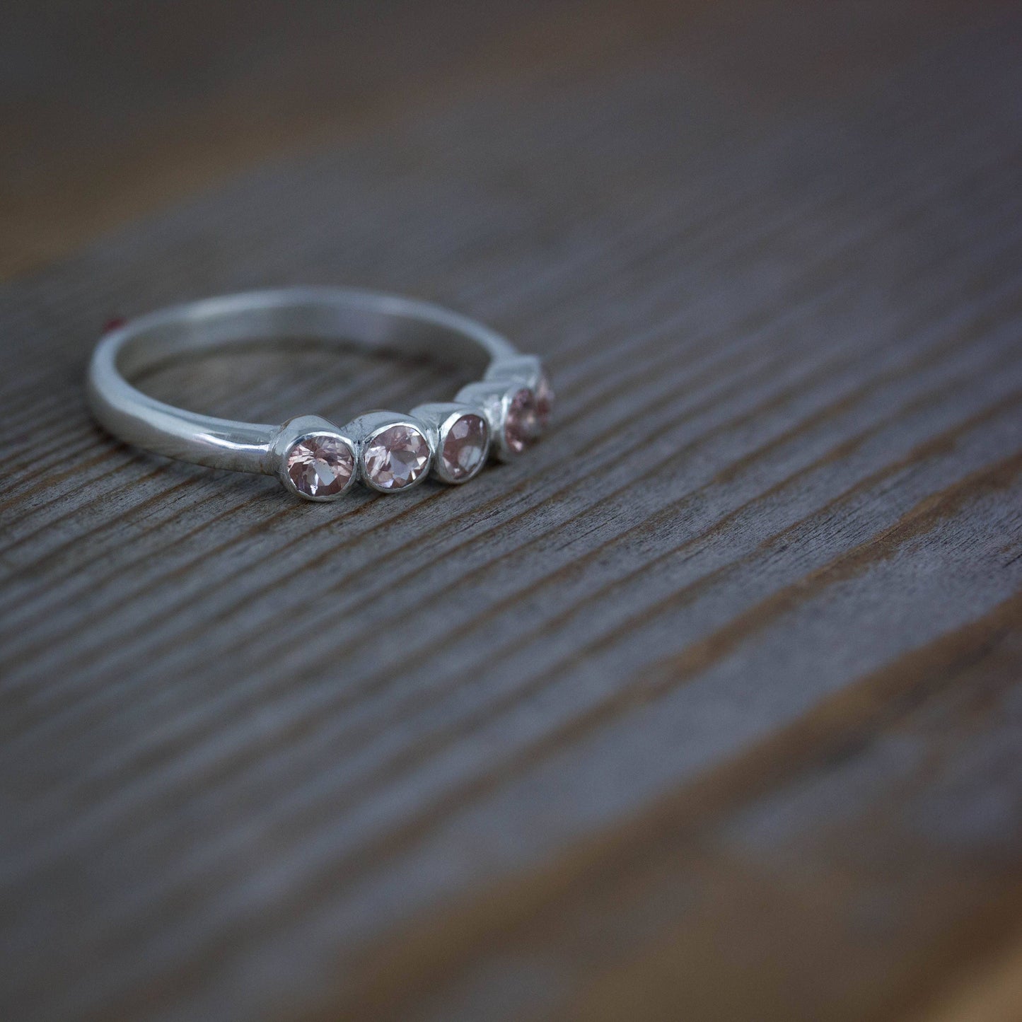 A handmade Silver Oregon Sunstone Band Ring with three pink stones on top of a wooden table from Cassin Jewelry.