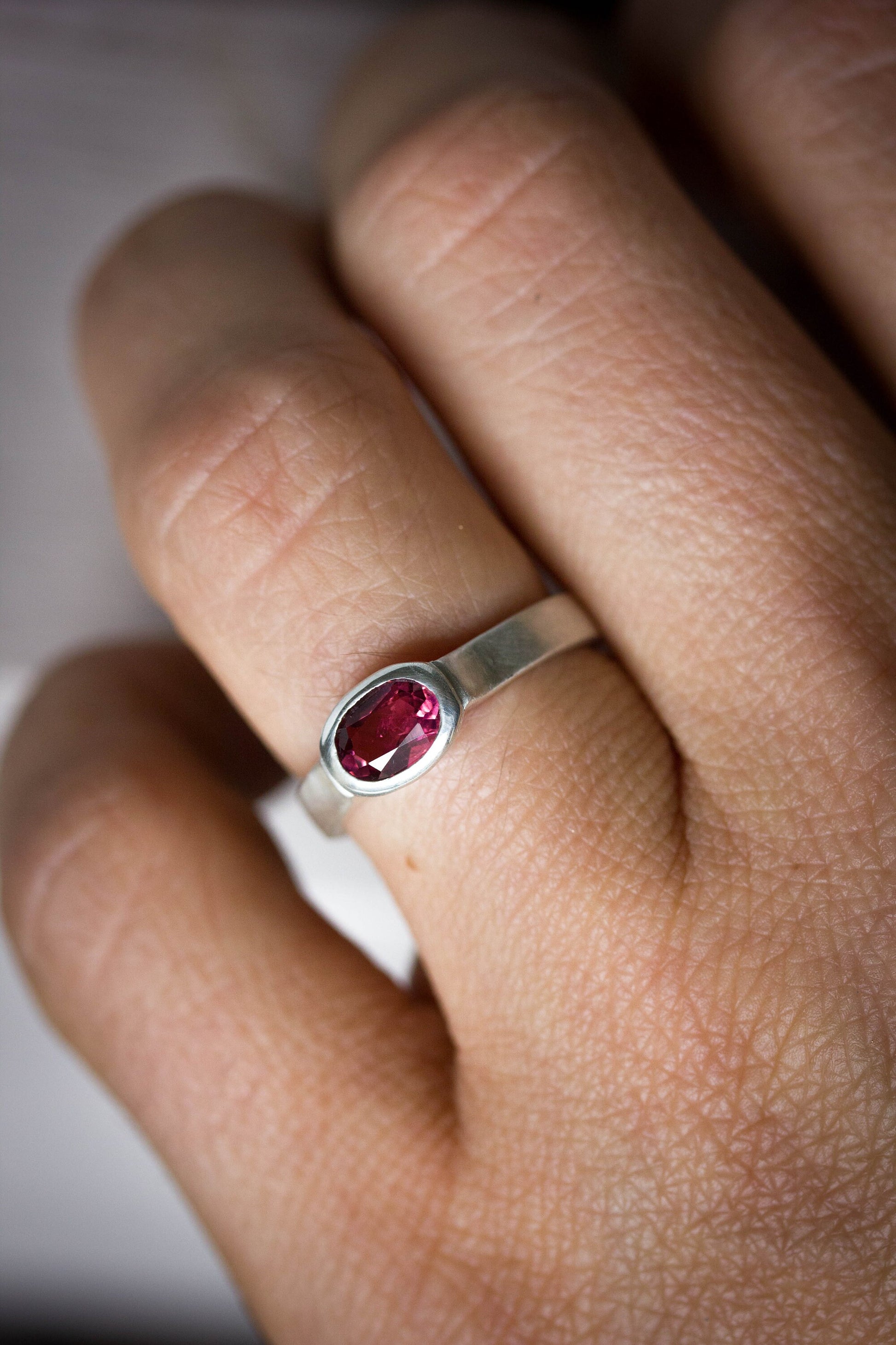 A handmade jewelry: A woman's hand holding a Pink Tourmaline Wide Band Ring, Brushed Silver With Low Profile, Size 7 Oval Gemstone Solitaire and October Birthstone.