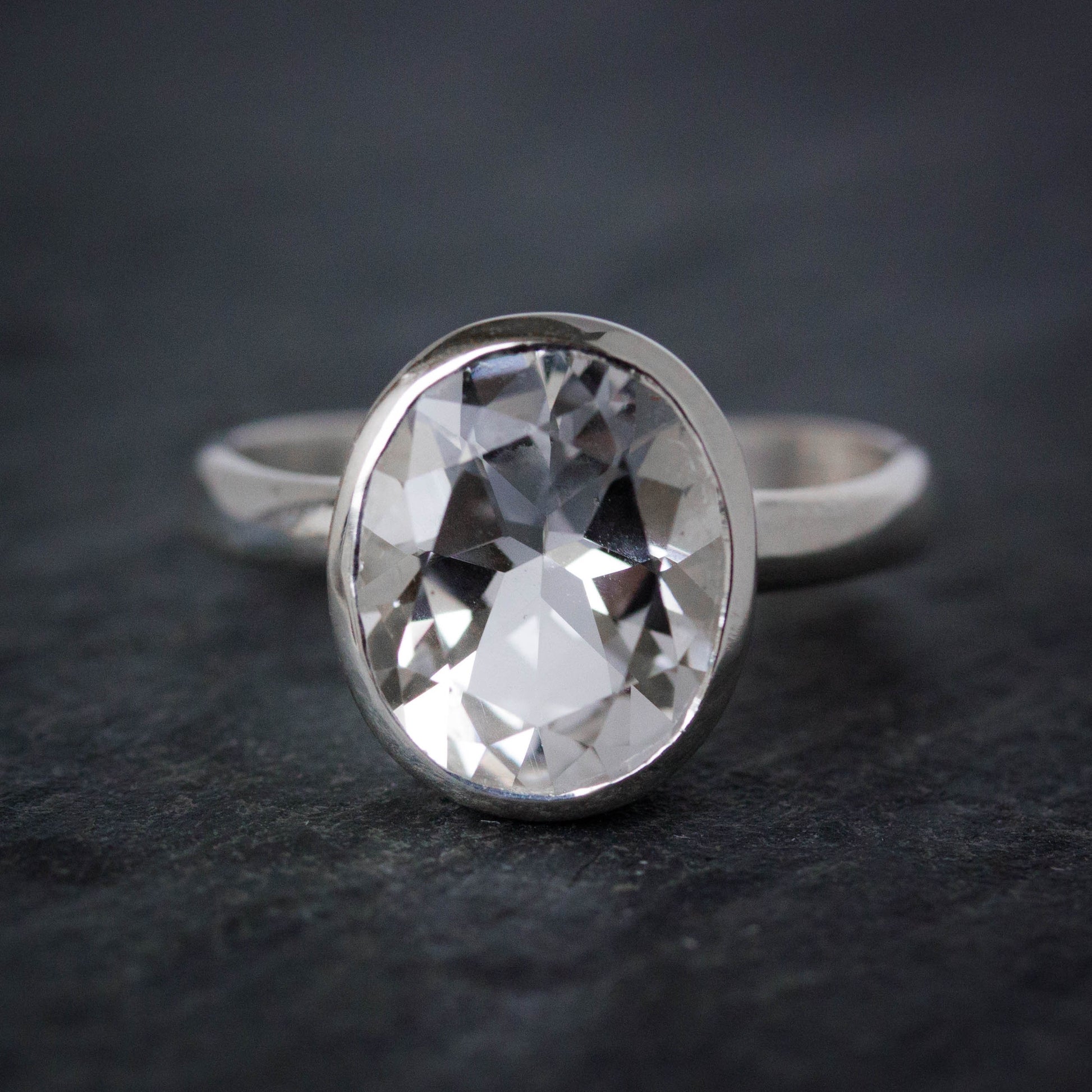 An Oval Size 6.5 Handcrafted White Topaz Ring on a black surface.