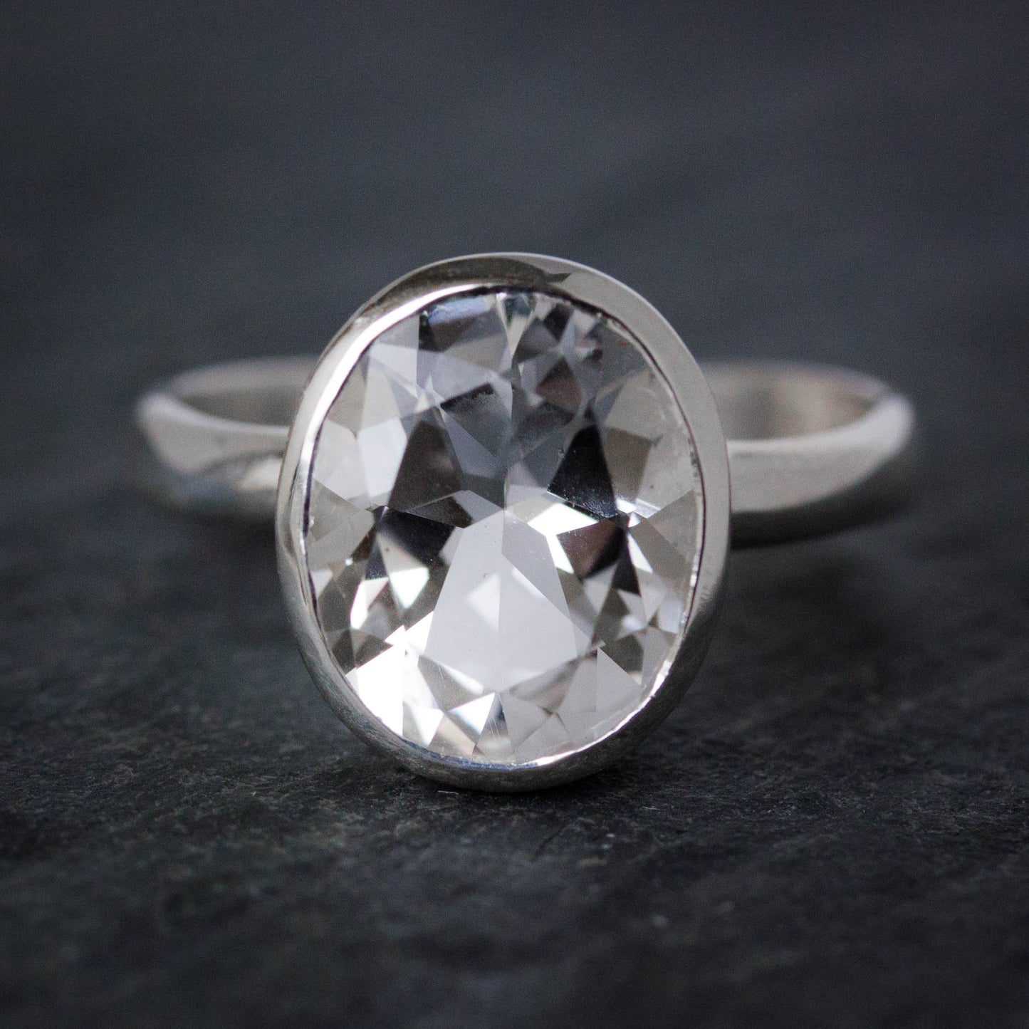 An eco-friendly Size 6.5 Handcrafted White Topaz ring, Oval Ring in Sterling Silver, Recycled Silver, with black surface showcasing the gemstone.