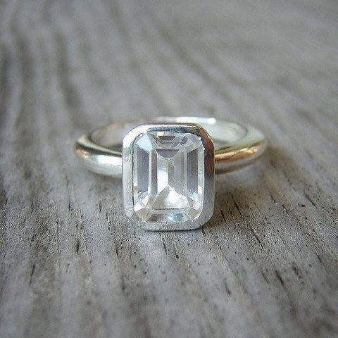 A handmade emerald white topaz gemstone ring from Cassin Jewelry, displayed on a wooden table.