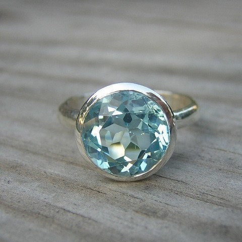 A handmade Sky Blue Topaz Birthstone Ring sitting on top of a wooden table.