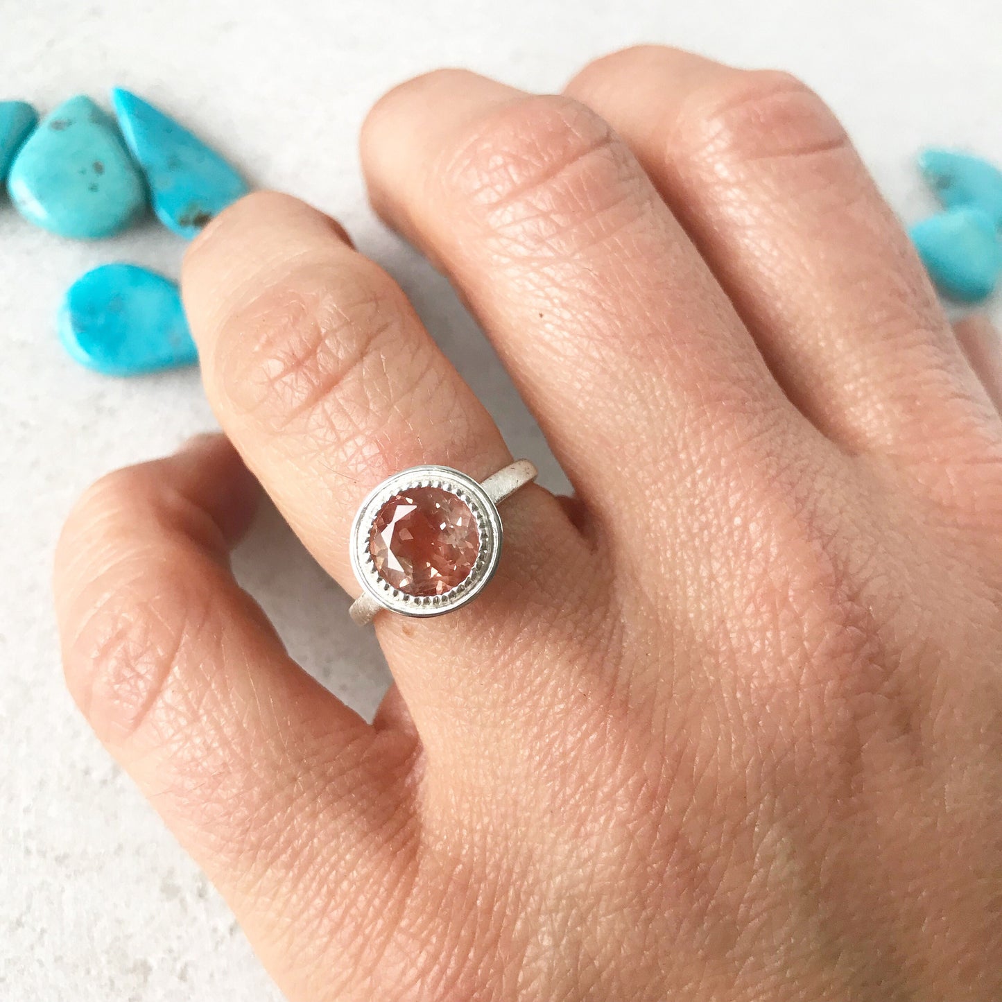 A woman's hand holding a handmade Oregon Sunstone Milgrain Ring in Brushed Sterling Silver by Cassin Jewelry.