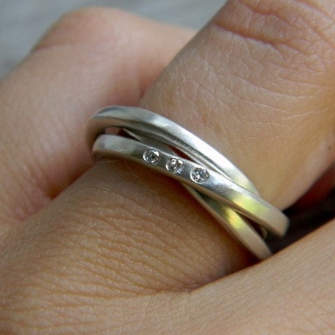 A woman's hand is holding a Silver Spinner Ring with Celtic Wedding Ring, Sterling Silver Rolling Ring, and Diamond Fidget Ring by Cassin Jewelry