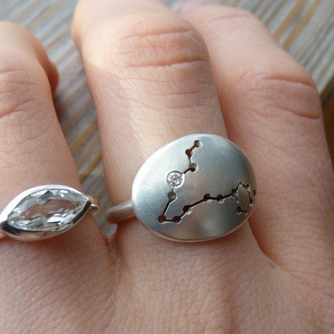 A woman's hand with a handmade Pisces constellation ring and a diamond.