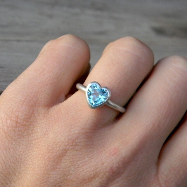 A woman's hand is holding a handmade pink heart shaped topaz ring.