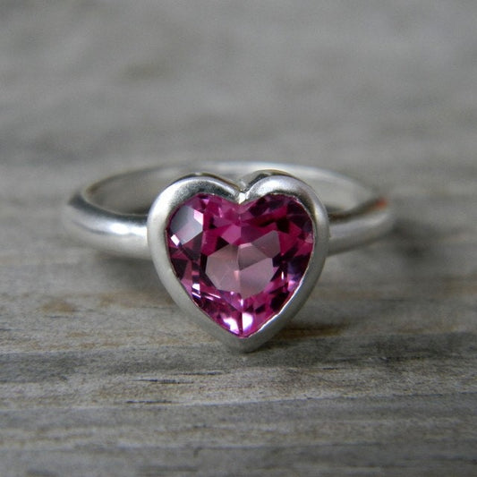 A Handmade Pink Heart Shaped Topaz Ring on a wooden surface.