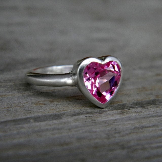 A handmade pink heart-shaped topaz ring on a wooden surface.