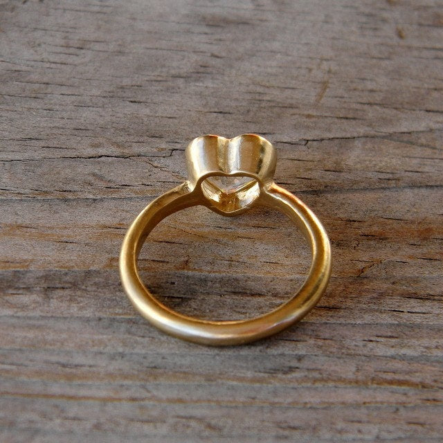 A Cassin handmade Heart Shaped White Topaz Ring in Yellow Gold on a wooden surface.