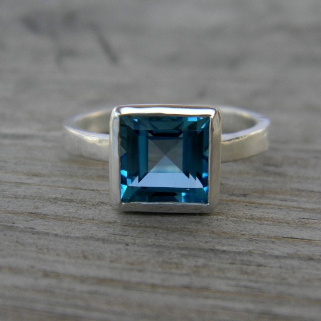 A Square London Blue Topaz Ring, Princess Cut Natural Topaz in Sterling Silver Bezel by Cassin Jewelry on a wooden table.