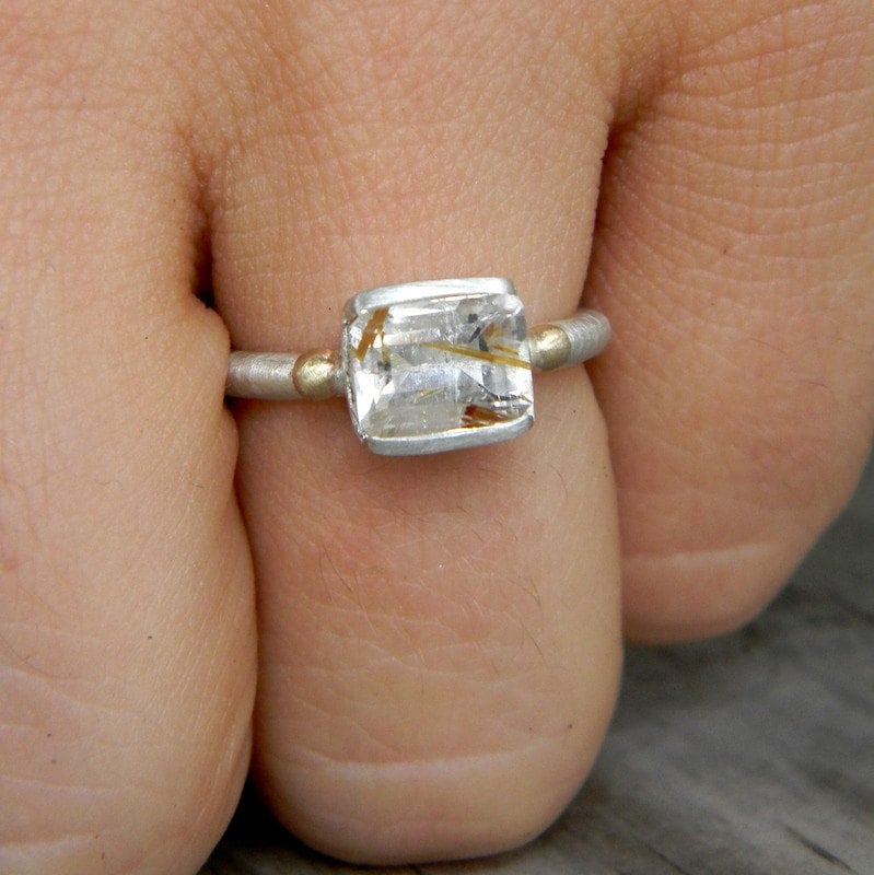A woman's hand is holding a handmade Emerald Cut Rutilated Quartz Ring in Mixed Metal by Cassin Jewelry.