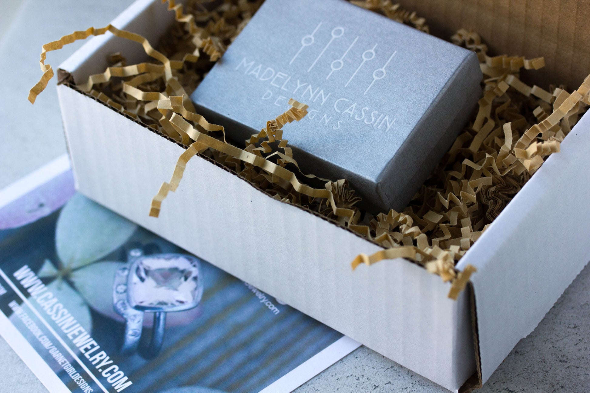 A box with a Handmade White Topaz Engagement Ring in it and a magazine by cassin jewelry.