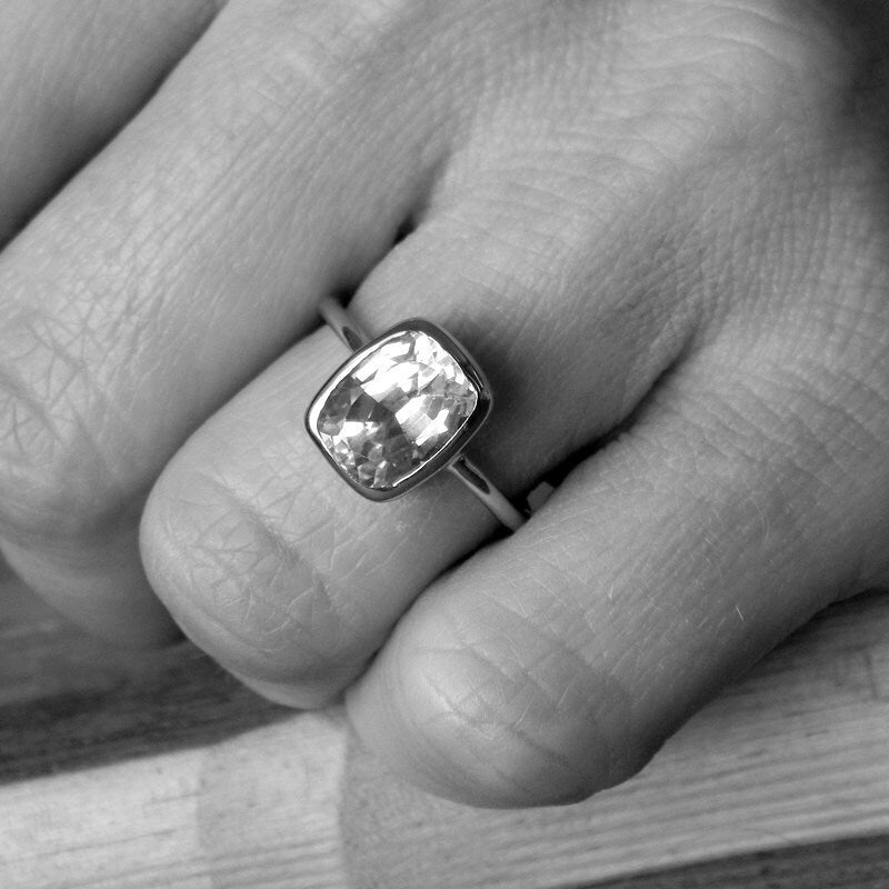 A black and white photo of a person wearing a Handmade White Topaz Engagement Ring from Cassin Jewelry.