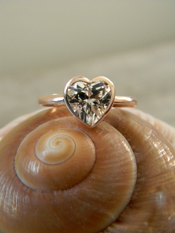 A Handmade Heart Shaped White Topaz Ring in Yellow Gold sitting on top of a shell.