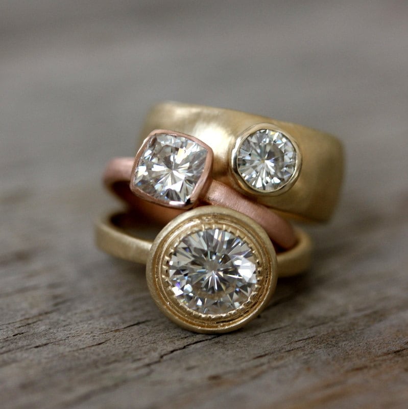 Three Cassin Jewelry handmade rose gold engagement rings on top of a wooden table.